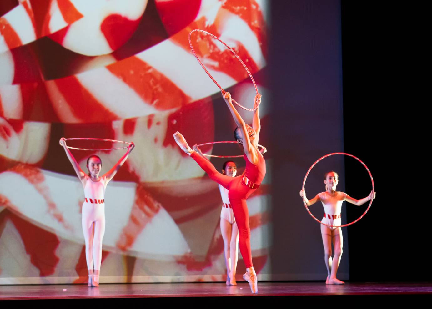 A young dancer in red executes a high attitude while holding a striped hoop